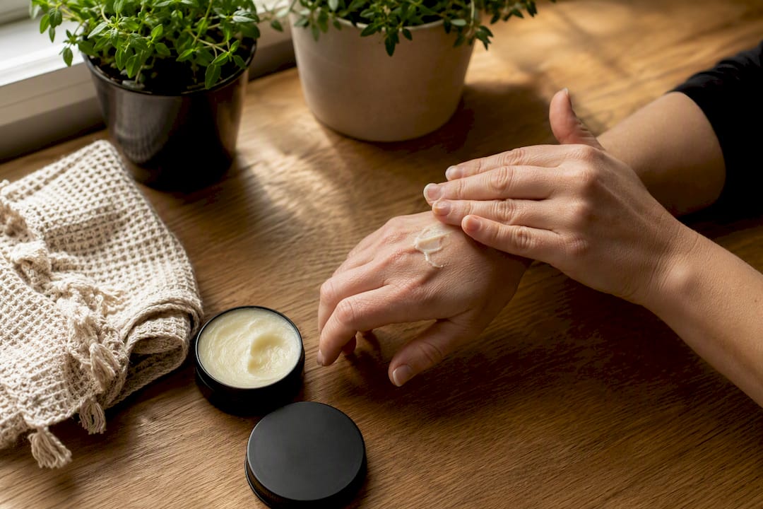 Hands applying tallow balm on forearm skin