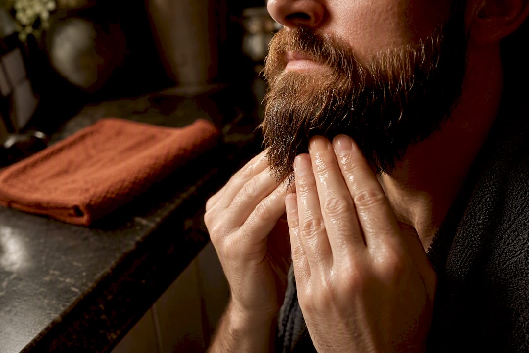 Hands smoothing balm through a damp beard
