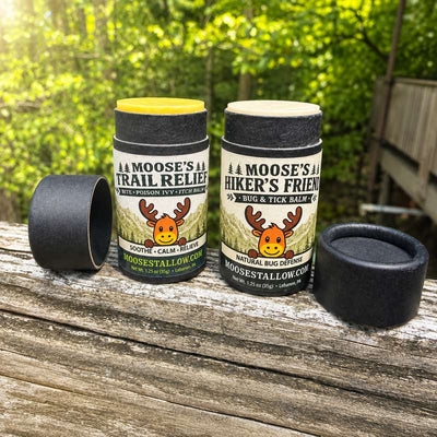 Moose's Trail Relief and Hiker's Friend outdoor balms on a wooden rail in the woods