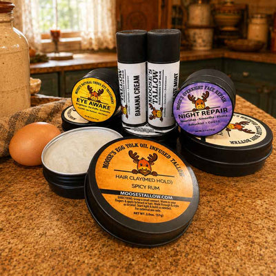 Moose's Egg Yolk Oil Infused Tallow products on a farmhouse counter with a raw egg: Hair Clay, Whipped Body Butter, Night Repair, and lip balms