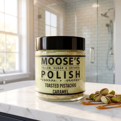Toasted Pistachio Caramel Sugar Scrub jar on a white marble bathroom counter with pistachios and caramel