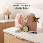 Natural diaper cream perfect for your diaper bag — Baby Bum Butter closed tin beside a pink diaper bag on the kitchen counter, ready to head out the door