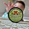 Baby holding Baby Moose's Baby Butter tin, calendula and chamomile infused