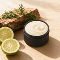 Bergamot and Cedar whipped tallow body butter in an open matte black tin beside sliced fresh bergamot and cedar wood