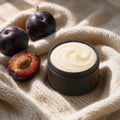 Cashmere & Plum whipped tallow body butter in a matte black tin on cream cashmere knit with ripe dark plums