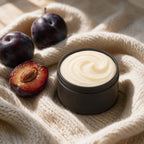 Cashmere & Plum whipped tallow body butter in a matte black tin on cream cashmere knit with ripe dark plums