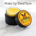 Open jar of Eye Awake tallow eye cream showing the yellow balm, with the lid beside it on white marble