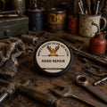 Beef tallow hand cream tin on a mechanic's workbench surrounded by greasy tools and wrenches