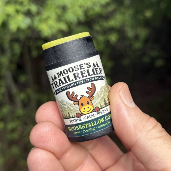 Hand holding Moose's Trail Relief bite, poison ivy & itch balm stick on a wooded trail